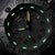 Gros plan d'une montre pour homme avec des aiguilles lumineuses et des index des heures verts et jaunes.