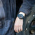Montre pour homme au poignet avec bracelet noir et cadran bleu et rouge
