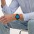 Armbanduhr am Handgelenk, schwarzes Band, blaues Zifferblatt an hellblauem Hemd.