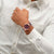 Armbanduhr am Handgelenk mit burgunderrotem Zifferblatt, geripptem Armband und Roségold.