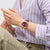 Armbanduhr am Handgelenk mit burgunderrotem Zifferblatt und geripptem Armband.