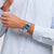 An Hand getragene Armbanduhr mit silbernem Metallband und blauem Zifferblatt