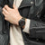 Armbanduhr mit schwarzem Chronograph-Zifferblatt und khakifarbenem Textilband am Handgelenk