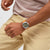 Swatch Herrenarmbanduhr am Handgelenk mit orangefarbenem Textilband und beigem Zifferblatt