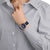 Montre unisexe au poignet, cadran bleu, boîtier argenté, bracelet en textile bleu foncé.
