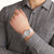 Montre-bracelet au poignet : boîtier gris, cadran gris, bracelet textile gris.