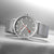 Montre homme avec bracelet milanais argenté et cadran gris, aiguille des secondes rouge.