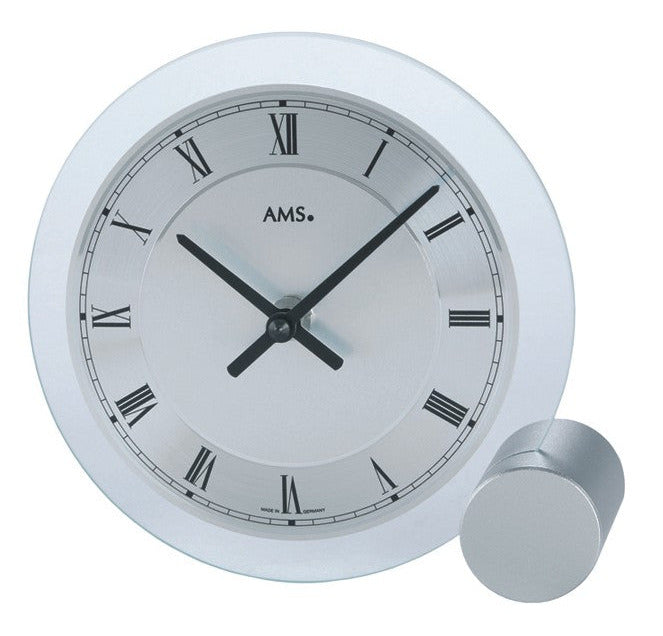 Horloge de table ronde avec cadre argenté, cadran blanc, chiffres romains et aiguilles noires.