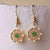 Paire de pendants d'oreilles dorés avec un insert rond vert et des pierres scintillantes.