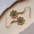 Boucles d'oreilles pendantes avec insert rond vert, design doré et pierres scintillantes.