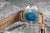 Montre pour homme avec bracelet en cuir marron ; logo bleu visible sur le fond du boîtier.
