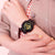 Montre pour femme en détail : bracelet noir avec cadran doré au poignet