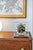 Horloge de table dans un boîtier en verre sur une commode en bois avec cadran rond et mouvement
