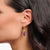 Boucle d'oreille créole dorée avec pendentif goutte violette à l'oreille