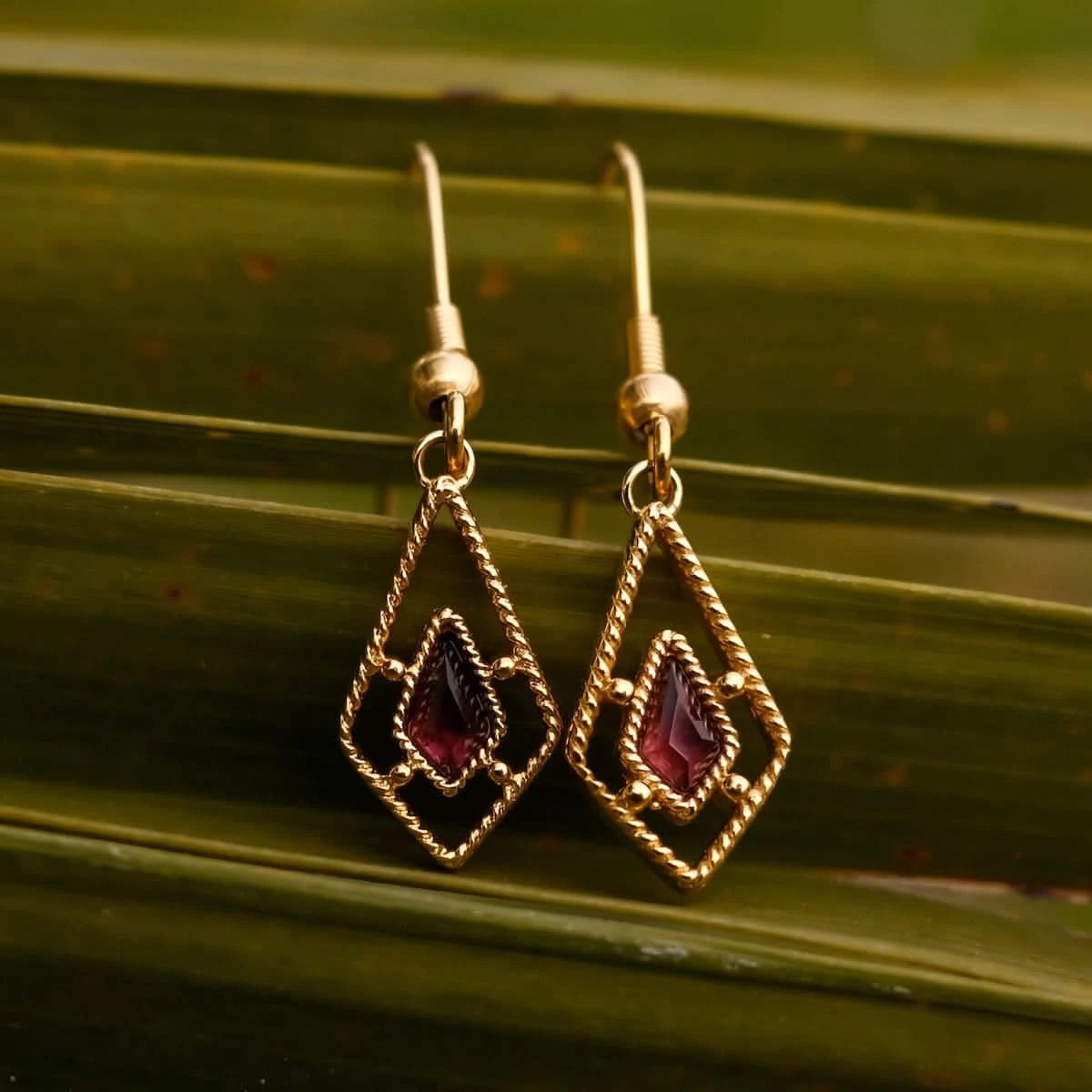 Boucles d'oreilles dorées avec pierre sombre dans un cadre carré en fil de fer, forme goutte.