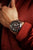 Chronographe pour homme avec cadran noir et détails rouges, porté avec des poignets en tricot rouge.