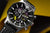 Montre homme en gros plan : cadran noir, boîtier argenté, bracelet en cuir noir