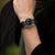Herrenarmbanduhr am Handgelenk mit schwarzem Textilband und schwarzem Zifferblatt
