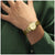 Damenuhr mit goldfarbenem Metallarmband am Handgelenk, rundes Zifferblatt