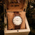 Holzkern-Armbanduhr in Holzhalterung: braunes Holzarmband, beiges Zifferblatt mit Zeigern