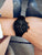 Schwarze Damenuhr am Handgelenk mit Metallarmband und schwarzem Chronographen-Zifferblatt