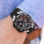 Montre pour homme au poignet : chronographe noir avec lunette et bracelet noir.