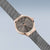 Montre femme vue de côté : lunette or rose, cadran gris foncé, bracelet milanais
