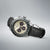 Bracelet de montre pour homme avec cadran beige et bracelet en cuir noir perforé.