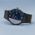 Montre homme de face, en biais : cadran bleu, lunette noire, bracelet en maille noire
