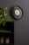 Horloge murale ronde sur un mur, cadre noir, cadran beige avec des marqueurs dorés.