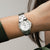 Damenuhr am Handgelenk mit silberfarbenem Metallarmband und weißem Zifferblatt