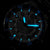 Montre homme dans l'obscurité : aiguilles et index luminescents bleus sur cadran noir
