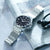 Montre bracelet pour homme au poignet avec cadran noir et bracelet en métal argenté.