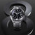 Montre bracelet pour homme de face avec cadran noir, boîtier argenté et bracelet en métal.