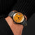 Montre pour homme au poignet : cadran orange, bracelet en cuir gris avec perforations décoratives