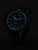 Montre homme avec cadran sombre et index verts lumineux, bracelet noir