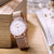 Damenuhr auf Holz: roséfarbene Mesh-Armbandkette mit rundem Gehäuse und weißem Zifferblatt