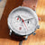 Montre homme, vue de biais : cadran blanc, bracelet en cuir marron, aiguilles rouges, chronographe