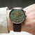 Montre pour homme au poignet : cadran vert, aiguilles orange et bracelet en cuir marron