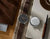 Montre homme avec bracelet en cuir marron sur un support, cadran rond noir