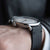 Herrenuhr am Handgelenk: schwarzes Lederarmband, silbernes Gehäuse und Krone.