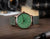 Montre homme sur bois : cadran vert, bracelet en cuir vert, lunette dorée rose.
