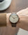 Montre pour homme au poignet : bracelet en cuir marron, cadran beige et boîtier en or rose.