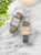 Deux montres pour femme style Tank avec cadran blanc, boîtier doré et bracelets en cuir (gris/beige).