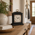 Horloge de table noire sur surface en bois, cadran blanc avec cadre floral, poignée dorée