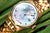 Montre pour femme avec lunette dorée, cadran bleu et index, affichage de la date à 5 heures.
