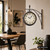 Wanduhr mit rundem Zifferblatt und schwarzem Metallbogen, an heller Wohnzimmerwand