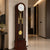 Pendule avec boîtier en bois foncé, cadran blanc et pendule dorée dans le verre
