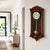 Wanduhr aus dunklem Holz mit Glasfront, goldenem Pendel und weißem Zifferblatt