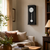Horloge murale sur un mur avec un boîtier noir, un cadran blanc et un poids de pendule rond